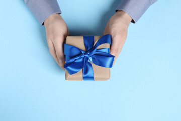 Man holding gift box with bow on light blue background, top view