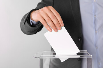 Man putting his vote into ballot box on light grey background, closeup