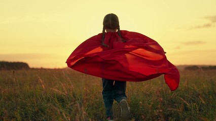 Cute little girl with braids wearing red cloak plays hero in sunset summer meadow