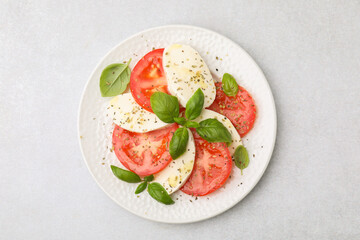 Plate of delicious Caprese salad with herbs on light grey table, top view