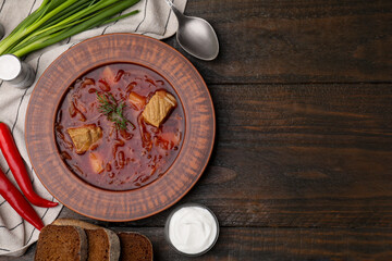 Bowl of delicious borscht, green onions, sour cream and chili peppers on wooden table, flat lay. Space for text