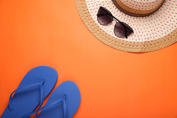 Stylish blue flip flops, sunglasses and hat on orange background, flat lay. Space for text