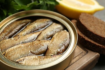 Tin can with tasty sprats served on wooden board, closeup