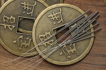 Acupuncture needles and Chinese coins on wooden table, flat lay