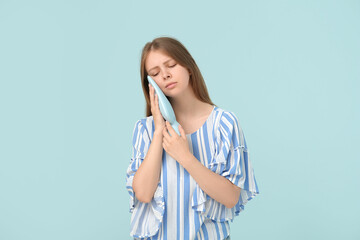 Young woman with tooth ache holding cold compress on blue background