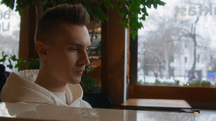 Young man alone drinks coffee in cafe. Stock footage. Handsome young man is drinking coffee alone. Man thoughtfully drinks coffee alone in cafe