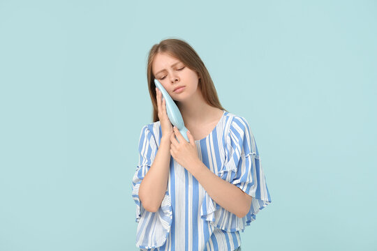 Young woman with tooth ache holding cold compress on blue background