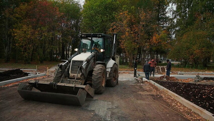 Tractor with workers working in city park. Clip. Workers with tractor dig ground in flower beds of...