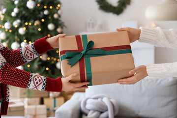 Woman receiving gift box from her friend at home on Christmas eve, closeup
