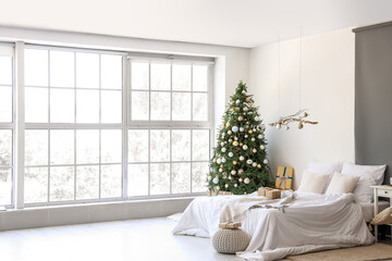 Interior of festive bedroom with comfortable bed, hanging decor and Christmas tree