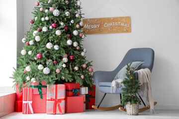 Gift boxes under Christmas tree and white armchair in festive room