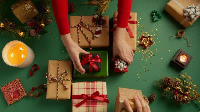 Female and male hands placing many colorful gift boxes on table. Flat layout full of beautiful present boxes on green background with Christmas decorations. Overhead view holiday gifts background 4K