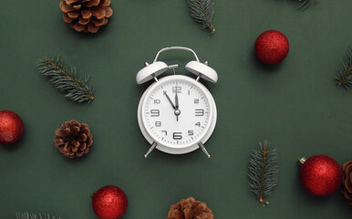 Alarm clock with Christmas tree branches and balls on green background