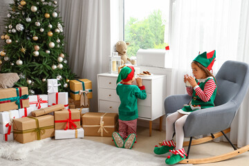Cute little children dressed as elves with milk and cookies at home on Christmas eve