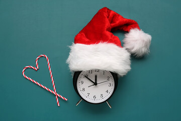 Composition with alarm clock, Santa hat and candy canes on color background