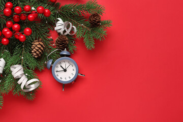 Alarm clock and Christmas tree branches with rowan on red background