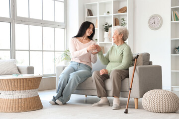 Senior woman taking glass of water from her daughter at home