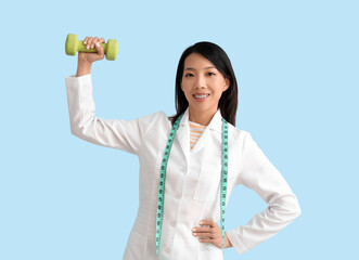 Female Asian nutritionist with dumbbell on blue background