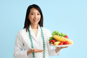 Female Asian nutritionist with vegetables on blue background