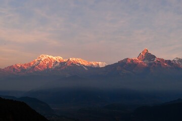 Capture the breathtaking beauty of the Annapurna ranges and the iconic Mt. Machapuchare bathed in a warm, red-hued sunrise as seen from the picturesque vantage point of Sarangkot near Pokhara, Nepal.