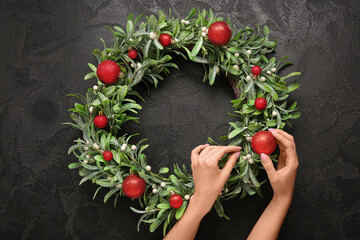 Woman making beautiful mistletoe wreath on black background