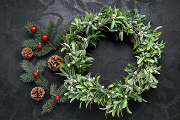 Beautiful mistletoe wreath with pine cones, fir branches and Christmas balls on black background
