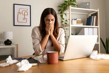 Fotobehang Sick woman working from home office. Caucasian female blowing nose with tissue while working with laptop. © Daniel