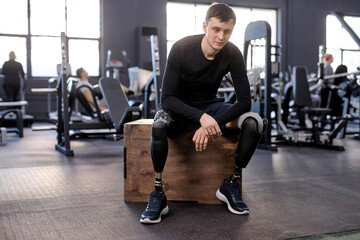 full length portrait of serious sportsman with prosthetic leg sitting on fitness box and after workout, free time, spare time. lifestyle, tiredness - obrazy, fototapety, plakaty