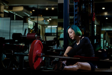 exhausted athletic asian woman after practicing routine weightlifting and overtrain at modern gym, active fitness people suffer pain injury accident from workout weight training in dark sport club