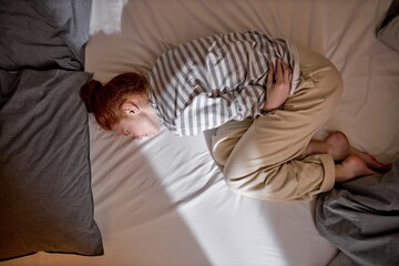 Top view of sick young ginger redhead woman lying in bed touch belly suffer from stomach ache, ill...