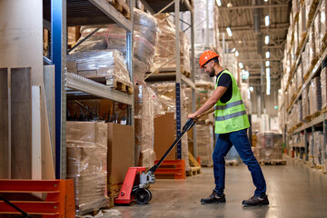 Young male warehouse worker carrying delivery to production stock using forklift. male staff in...