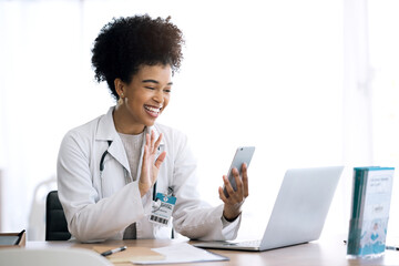 Doctor, woman and video call or phone communication in healthcare, social media or telehealth service at office. Happy african person or medical worker wave hello or talking on mobile voip for advice - obrazy, fototapety, plakaty