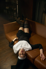 Sensual young nun with eyes closed wearing sexual lingerie lying on couch