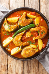 Indian cuisine Bengali Fish Curry Macher Jhol closeup on the plate on the wooden table. Vertical top view from above