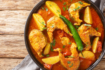 Machher jhol or machha jhola, is a traditional spicy fish curry in Bengali and Odia cuisines closeup on the plate on the wooden table. Horizontal top view from above