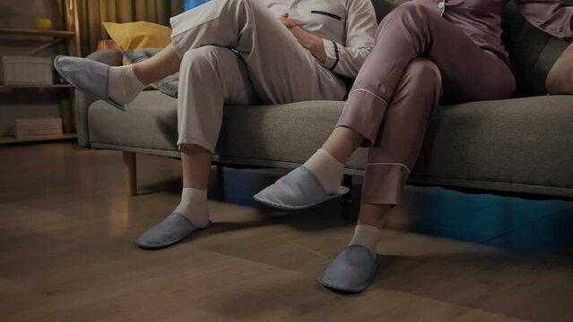 Portrait of young couple spending time together. Closeup shot of man and woman sitting on the sofa in pajamas and slippers and similar crossing legs .
