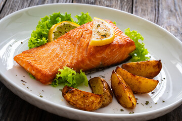 Seared salmon steak with baked potatoes and fresh vegetable salad served on wooden table
