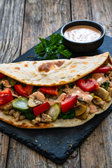 Italian piada wraps - piadina filled with mozzarella cheese, fried pork and vegetables and on wooden table
