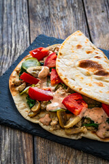 Italian piada wraps - piadina filled with mozzarella cheese, fried pork and vegetables and on wooden table

