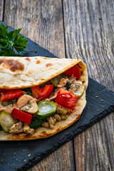 Italian piada wraps - piadina filled with mozzarella cheese, fried pork and vegetables and on wooden table
