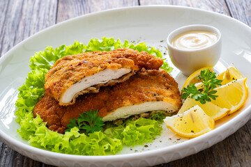 Crispy breaded seared chicken cutlet with lemon slices and fresh vegetables on wooden table
