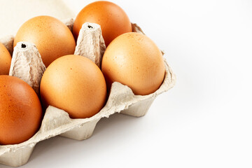 A tray of brown fresh hens eggs on white background. Eco-friendly egg production. Baking ingredients. Organic chicken eggs - fresh from producer. Top view.