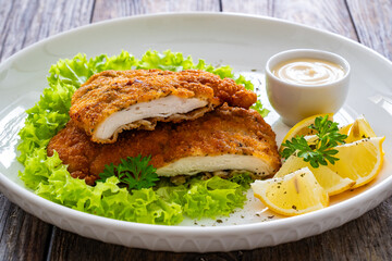 Crispy breaded seared chicken cutlet with lemon slices and fresh vegetables on wooden table
