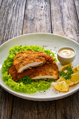 Crispy breaded seared chicken cutlet with lemon slices and fresh vegetables on wooden table
