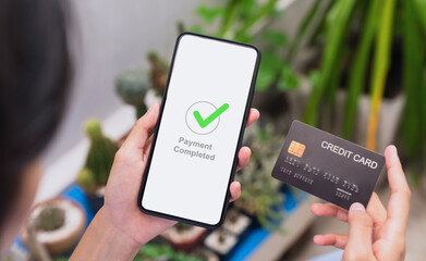 Hands holding smartphone with credit card and showing payment completed message on mobile.