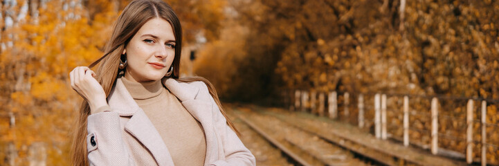 beautiful long-haired woman walks through the autumn streets. Railway, autumn, woman in a coat.