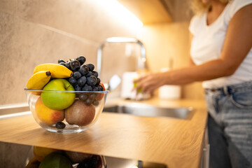 Bowl of healthy fresh fruit while in background woman washing apples.