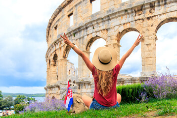 Ancient roman amphitheatre in Pula, Croatia- young female tourist with flag and bag enjoying arena...