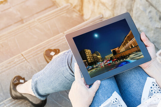 Lady holding tablet pc with picture of a big city at night, sitting on the stairs on a sunny day