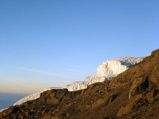 Fototapeta premium A rocky mountain slope behind which is an iceberg on the background of a blue sky